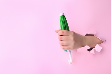 Photo of Woman holding closed small green umbrella through hole in light pink paper, closeup. Space for text