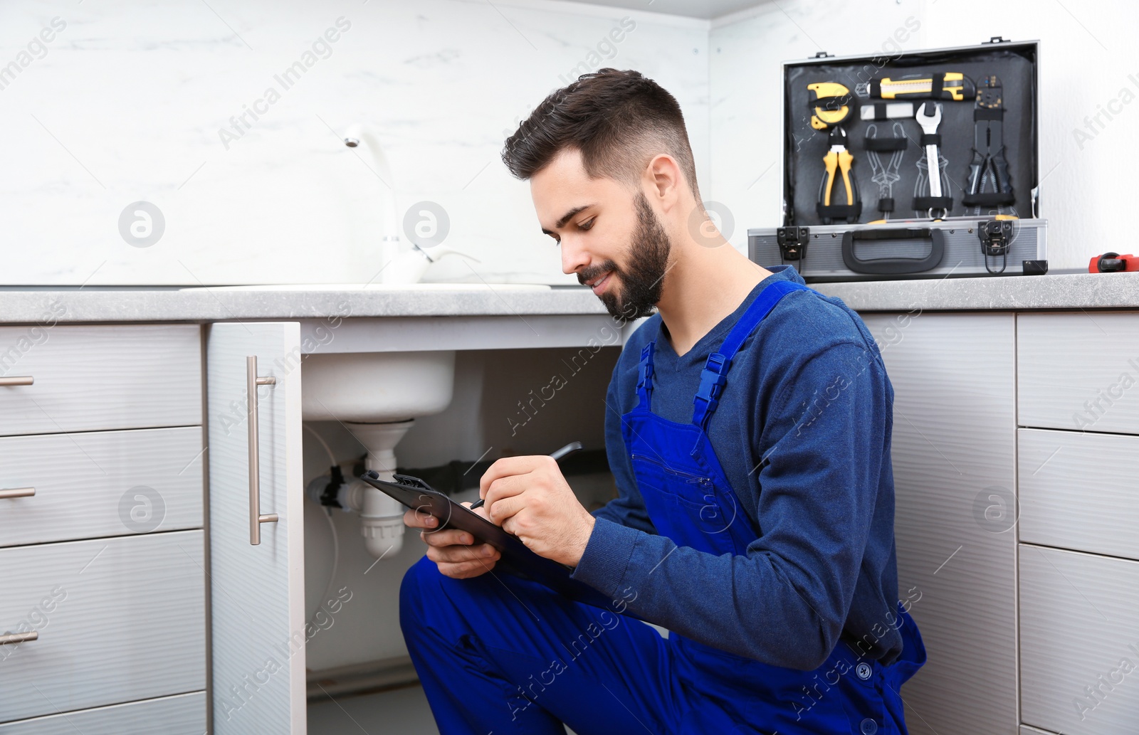 Photo of Male plumber with clipboard near kitchen sink. Repair service