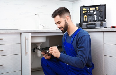 Photo of Male plumber with clipboard near kitchen sink. Repair service