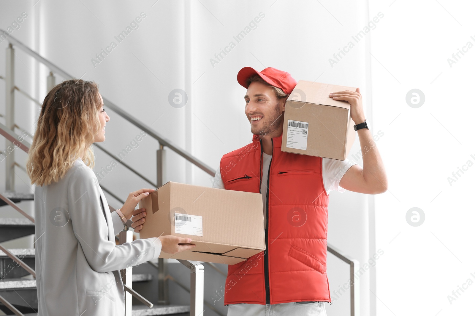Photo of Young woman receiving parcel from courier indoors
