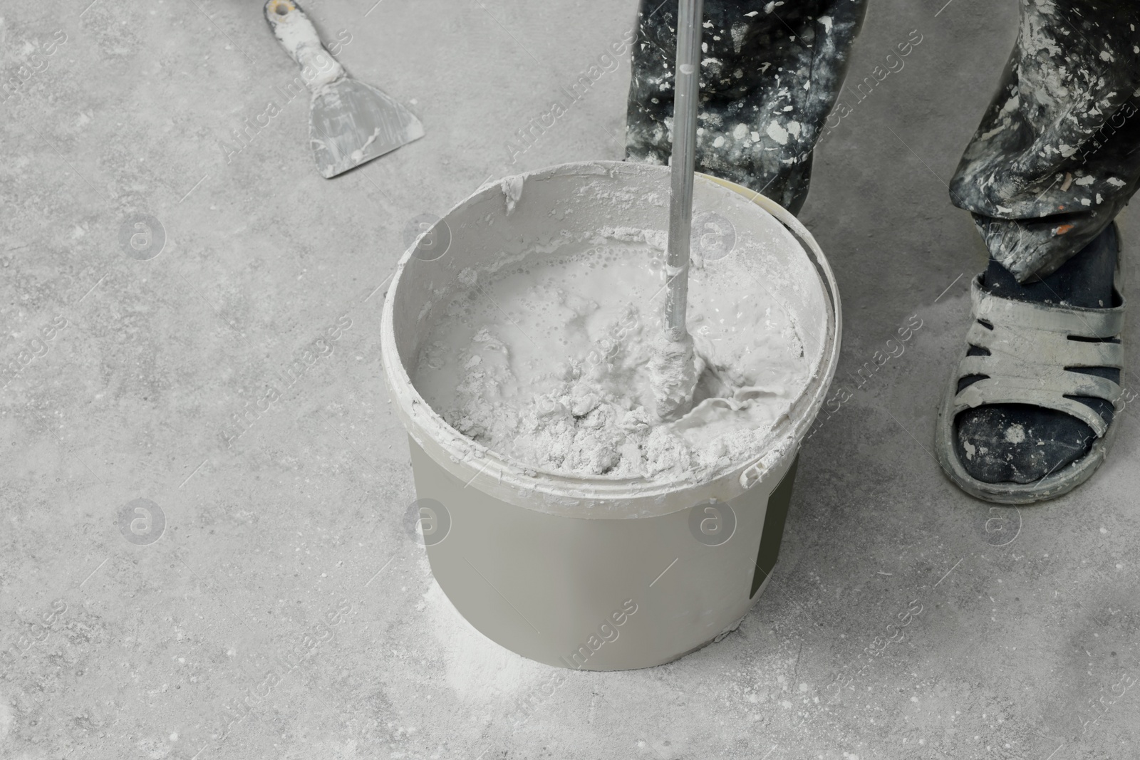 Photo of Professional worker mixing plaster in bucket indoors, closeup