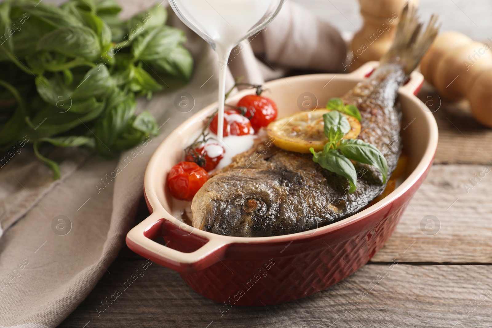 Photo of Pouring sauce into baking pan with delicious roasted dorado fish on wooden table, closeup