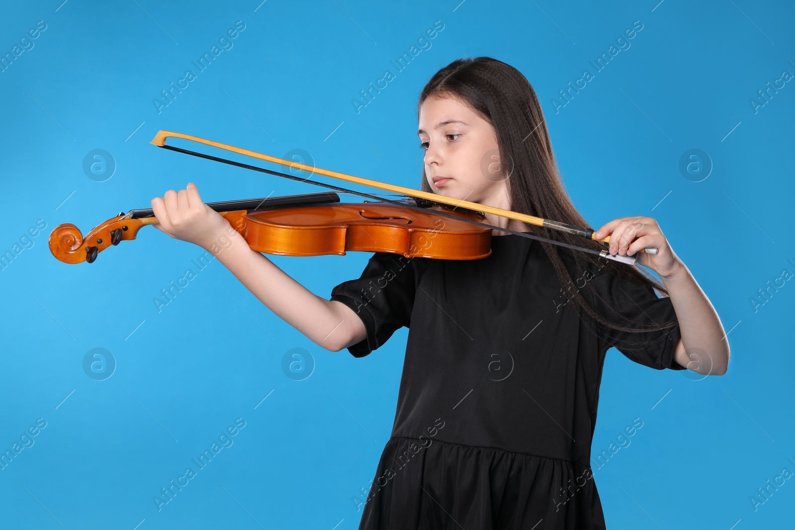 Photo of Preteen girl playing violin on light blue background