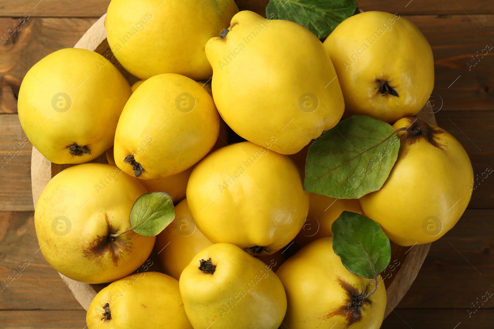 Photo of Tasty ripe quince fruits in bowl on wooden table, top view