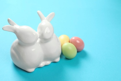 Photo of Ceramic Easter bunnies and dyed eggs on color background, space for text