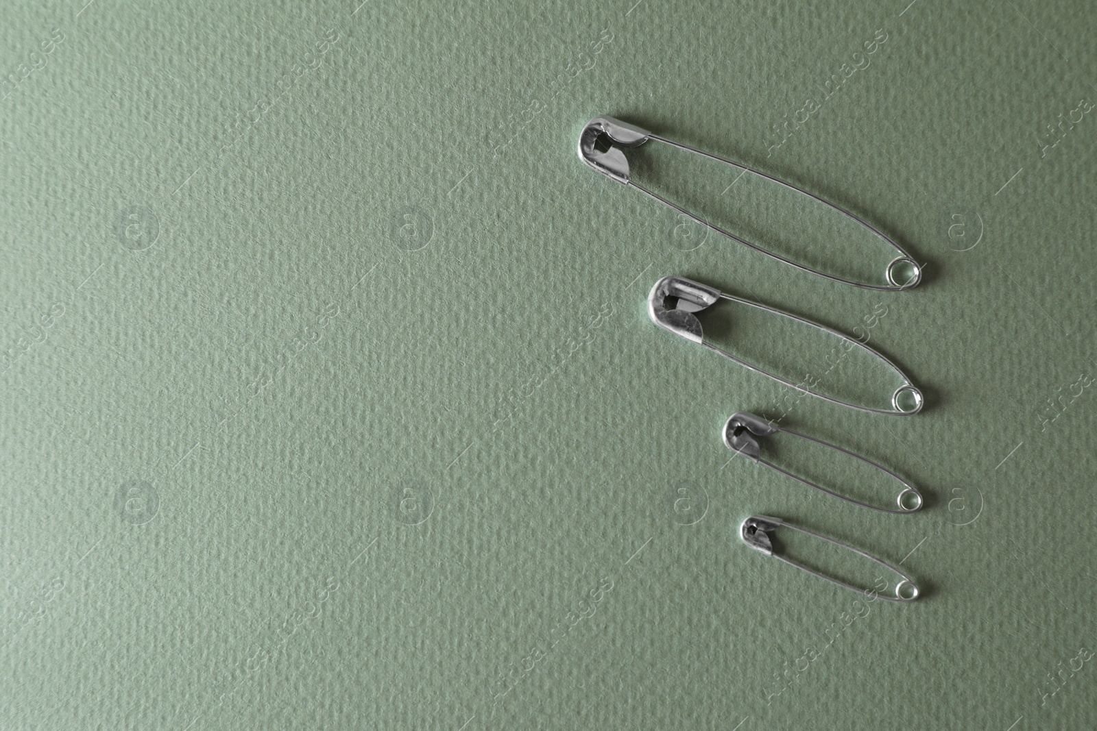 Photo of Different safety pins on green background, flat lay. Space for text