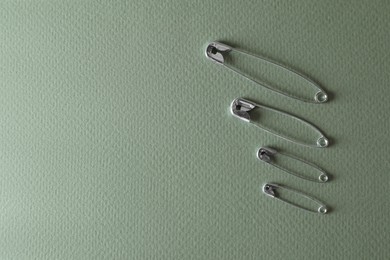 Different safety pins on green background, flat lay. Space for text