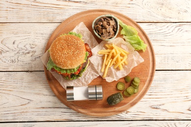 Photo of Board with tasty burger, french fries and vegetables on wooden table, top view