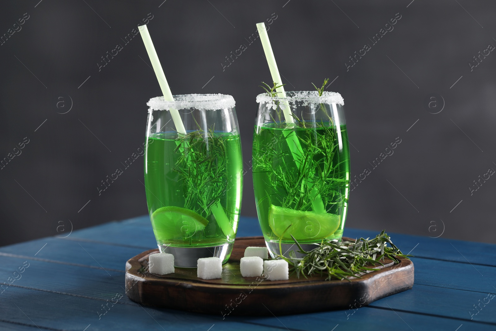 Photo of Glasses of homemade refreshing tarragon drink, sprigs and sugar cubes on blue wooden table