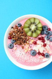 Photo of Tasty smoothie bowl with fresh kiwi fruit, berries and granola on light blue background, top view