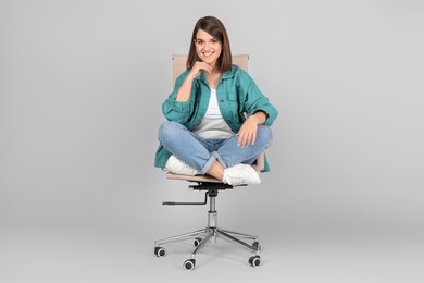 Photo of Young woman sitting in comfortable office chair on grey background