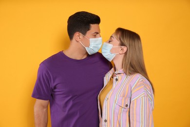 Couple in medical masks trying to kiss on yellow background