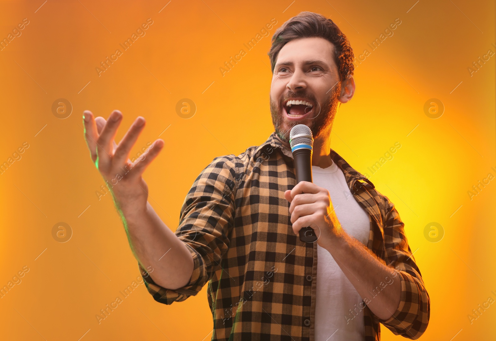 Photo of Handsome man with microphone singing on golden background