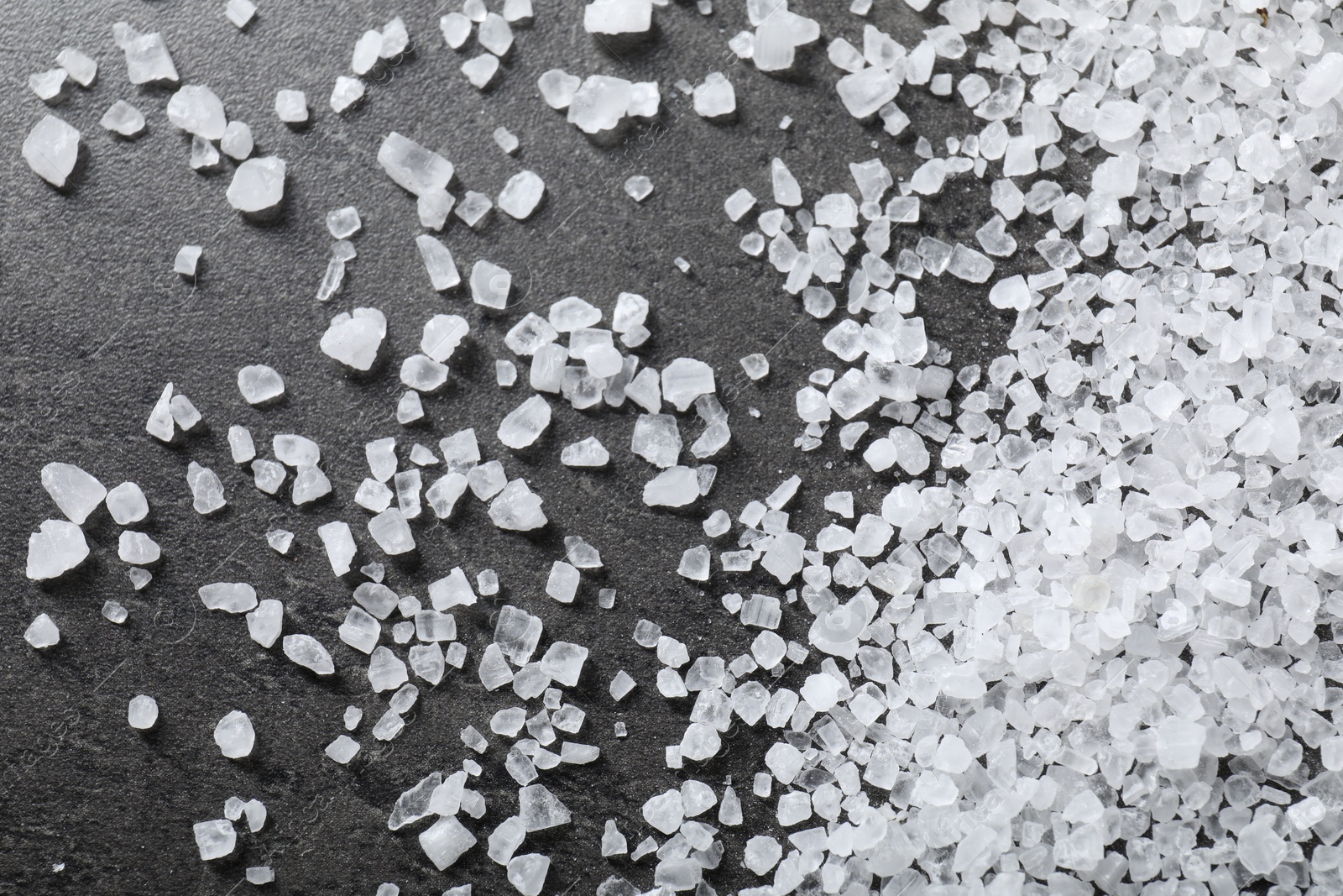 Photo of Scattered white natural salt on black table, top view