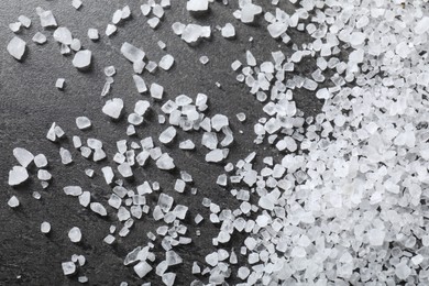 Scattered white natural salt on black table, top view