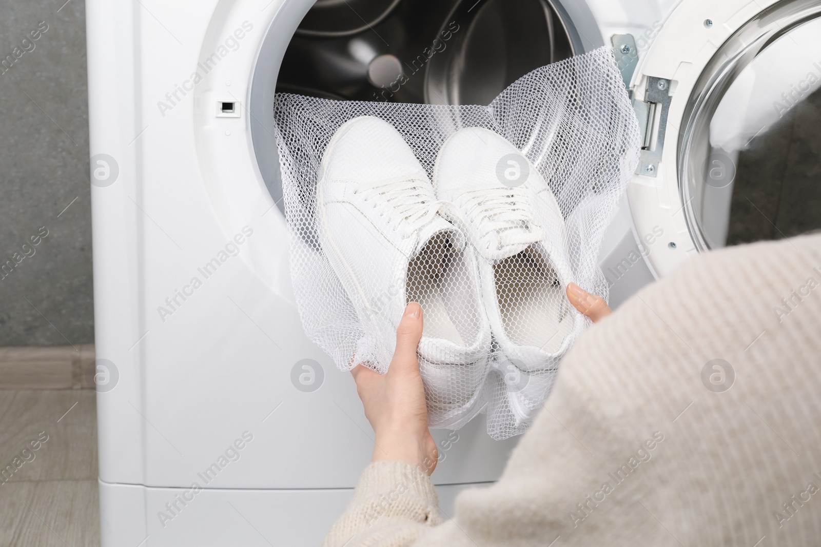 Photo of Woman putting stylish sneakers into washing machine, closeup