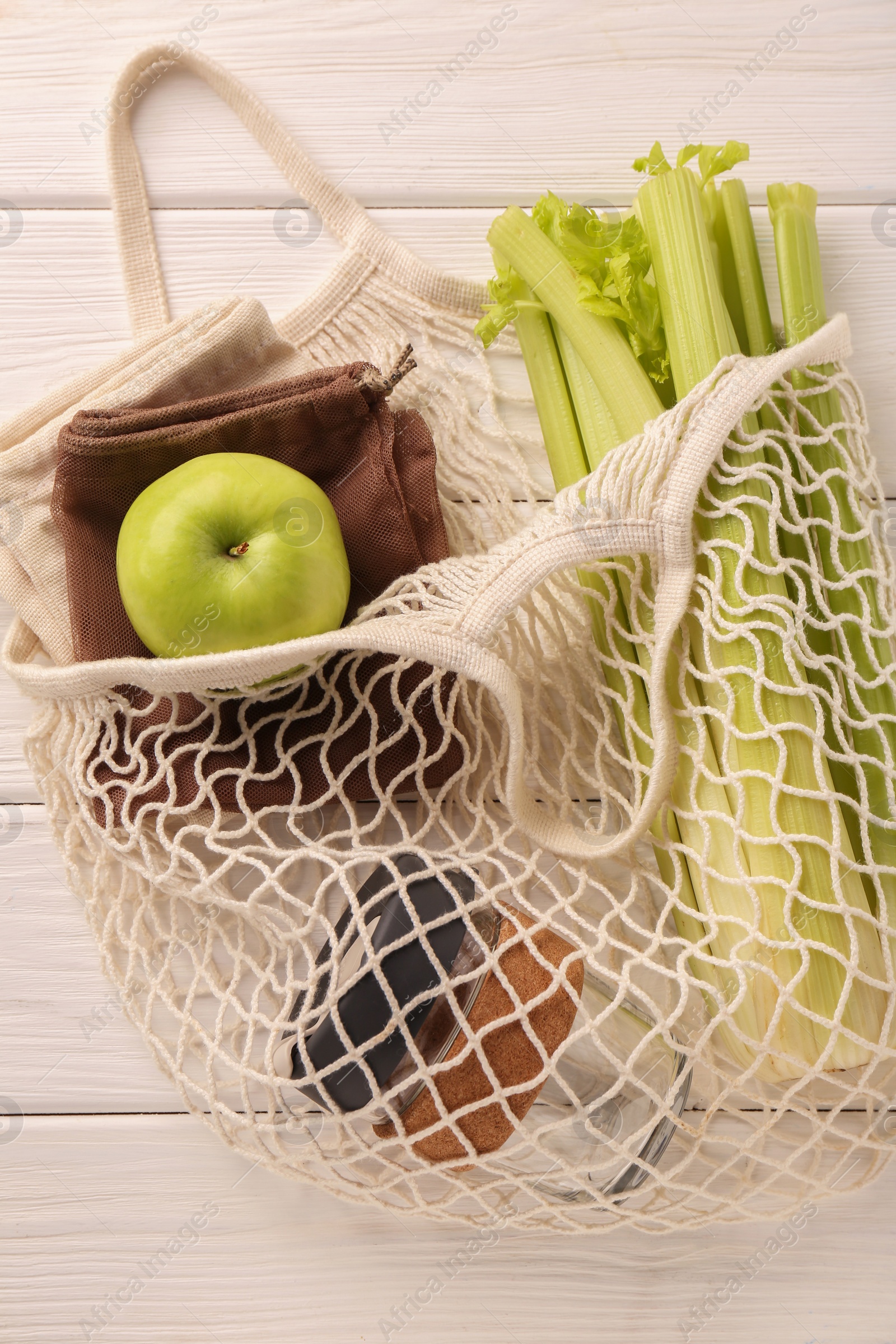 Photo of Net bag with different items on white wooden table, top view. Conscious consumption