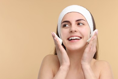 Photo of Young woman with headband washing her face on beige background, space for text