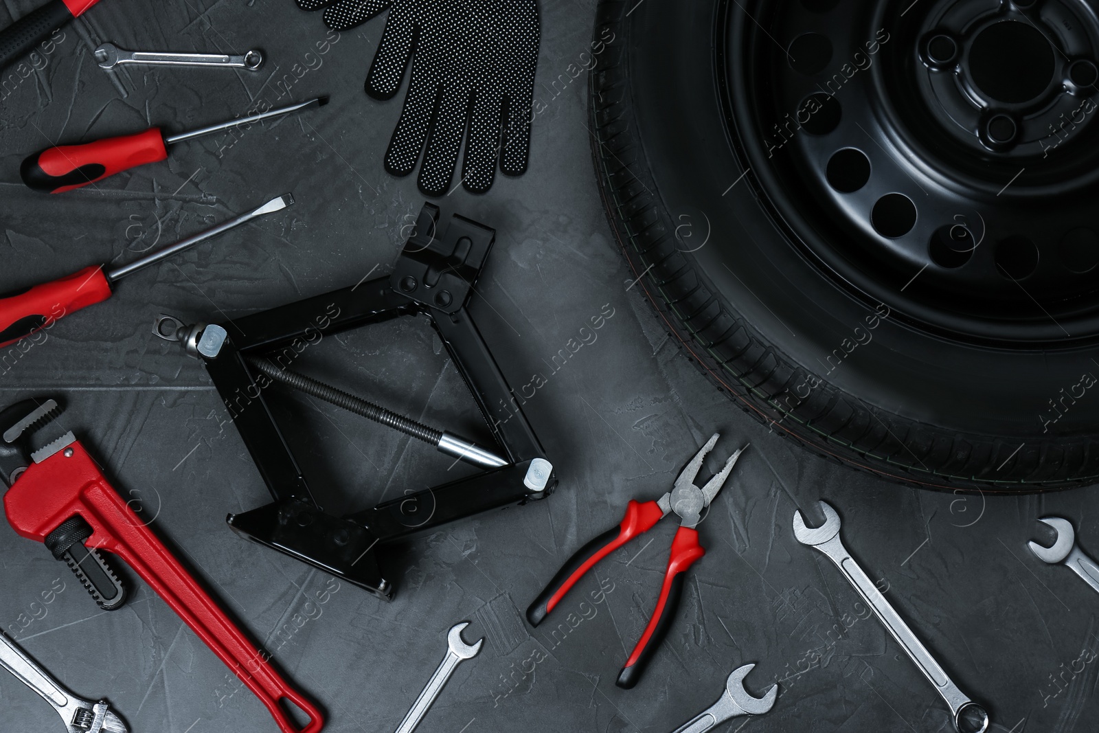 Photo of Car wheel, scissor jack and different tools on dark grey surface, flat lay