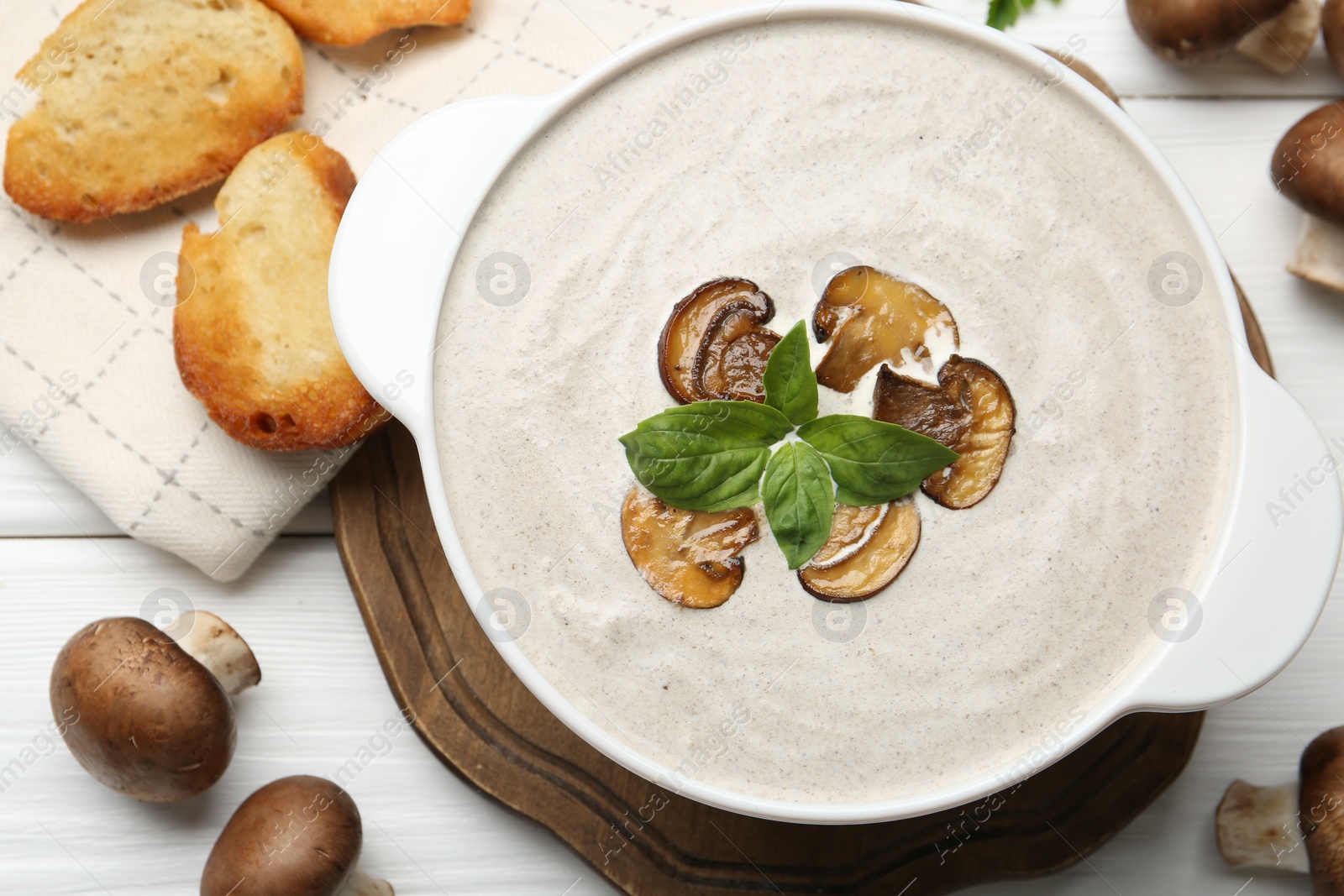 Photo of Delicious homemade mushroom soup in ceramic pot, croutons, fresh champignons and parsley on white wooden table, flat lay