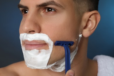 Photo of Handsome man shaving with razor on blue background, closeup