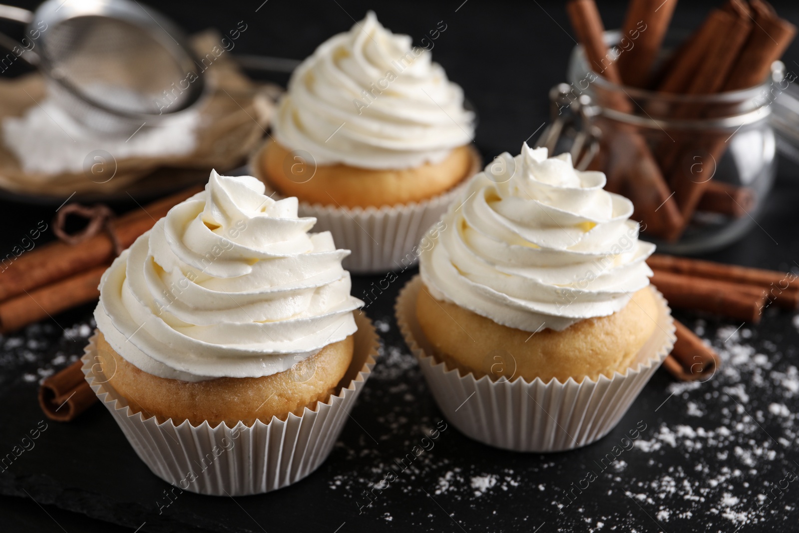 Photo of Delicious cupcakes with cream and cinnamon on black table, closeup