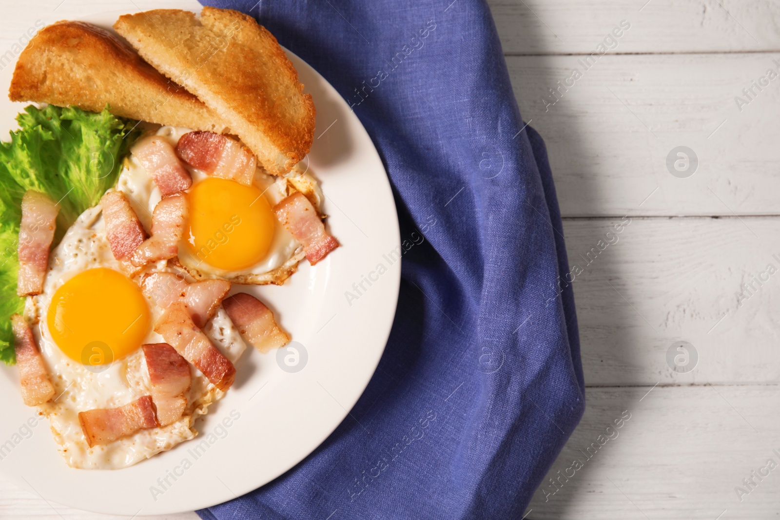 Photo of Fried eggs with bacon and toasted bread on plate served for breakfast, top view