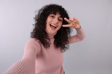 Beautiful young woman taking selfie on light grey background