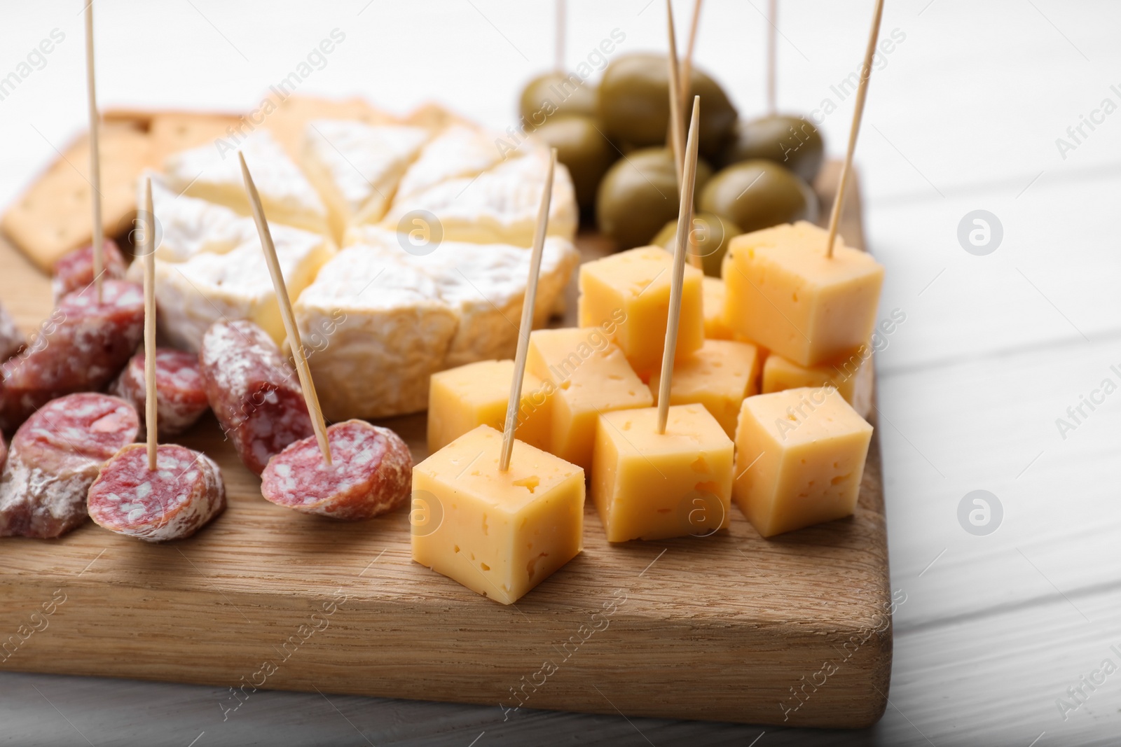 Photo of Toothpick appetizers. Pieces of sausage and cheese on wooden board, closeup