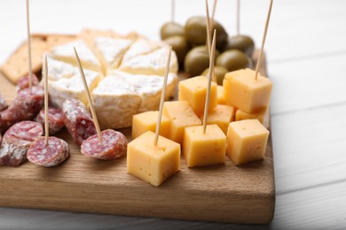 Photo of Toothpick appetizers. Pieces of sausage and cheese on wooden board, closeup