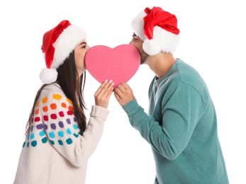 Photo of Young couple in Santa hats with heart shaped gift box on white background. Christmas celebration