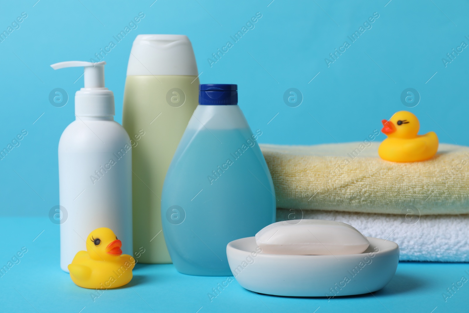 Photo of Baby cosmetic products, bath ducks and towels on light blue background