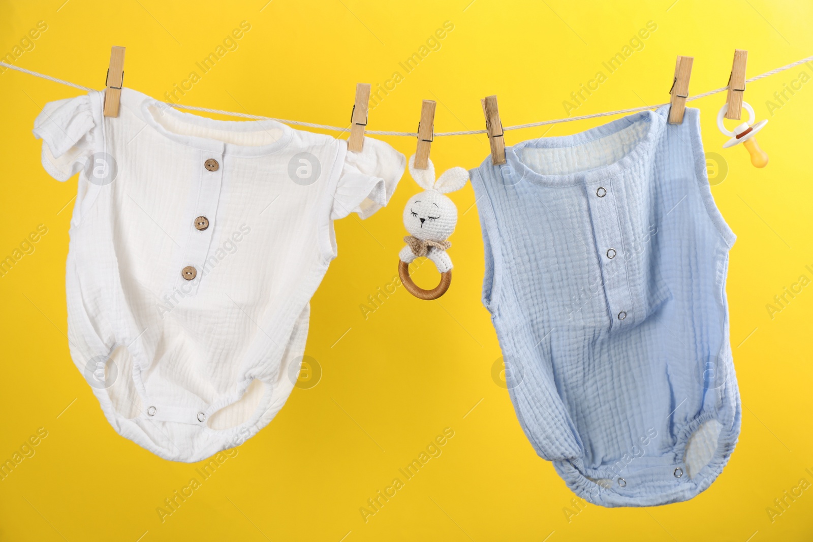 Photo of Baby clothes and accessories hanging on washing line against yellow background
