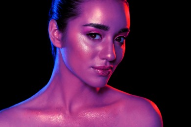 Image of Portrait of beautiful woman with glitter makeup in neon lights against black background