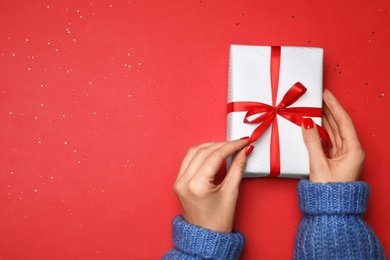 Young woman holding Christmas gift on red background, top view. Space for text