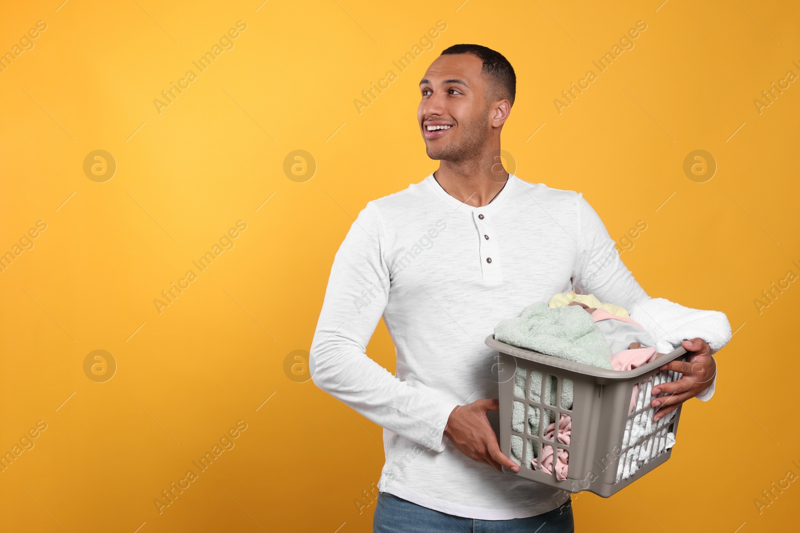 Photo of Happy man with basket full of laundry on orange background. Space for text