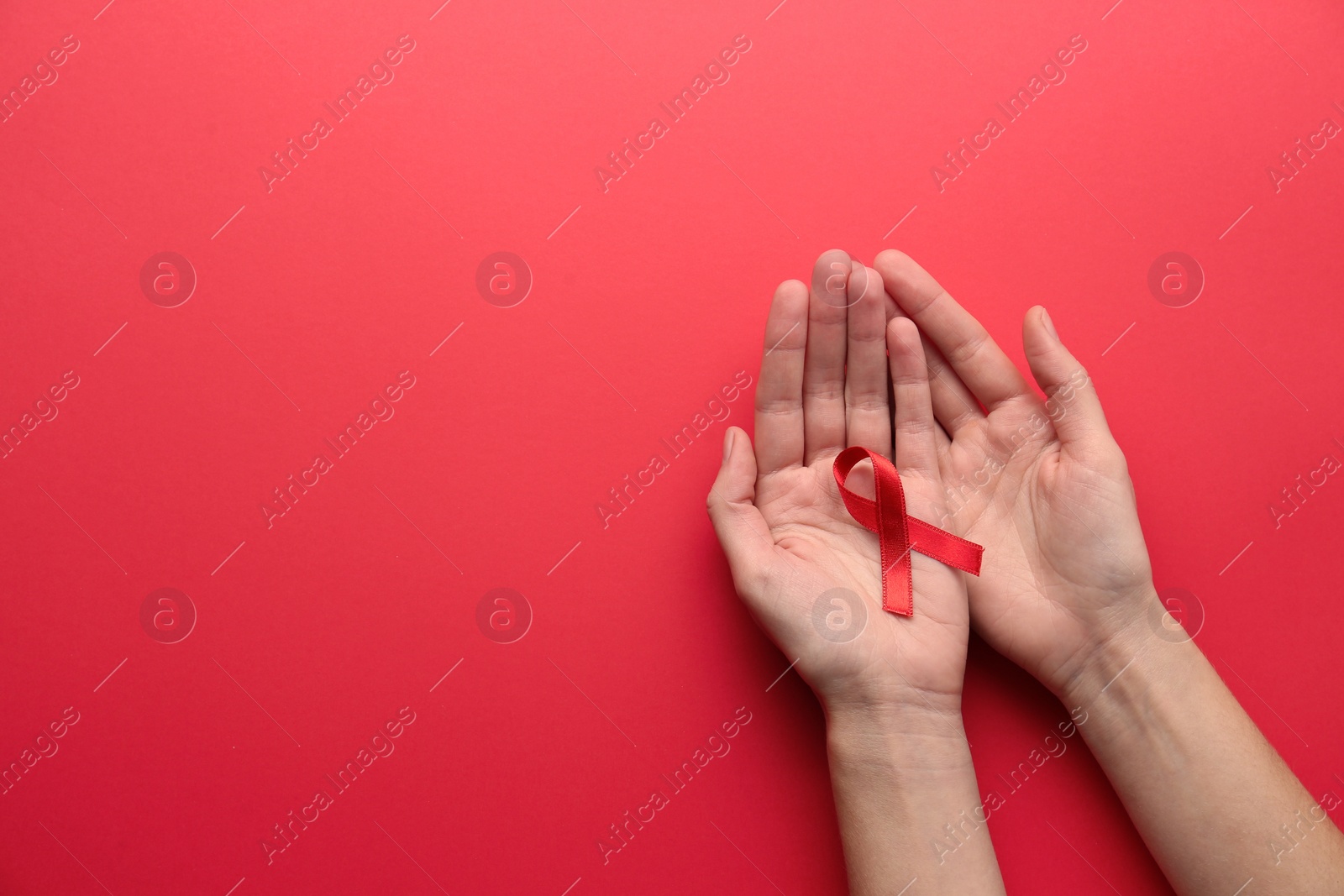 Photo of Woman holding red awareness ribbon on color background, top view with space for text. World AIDS disease day