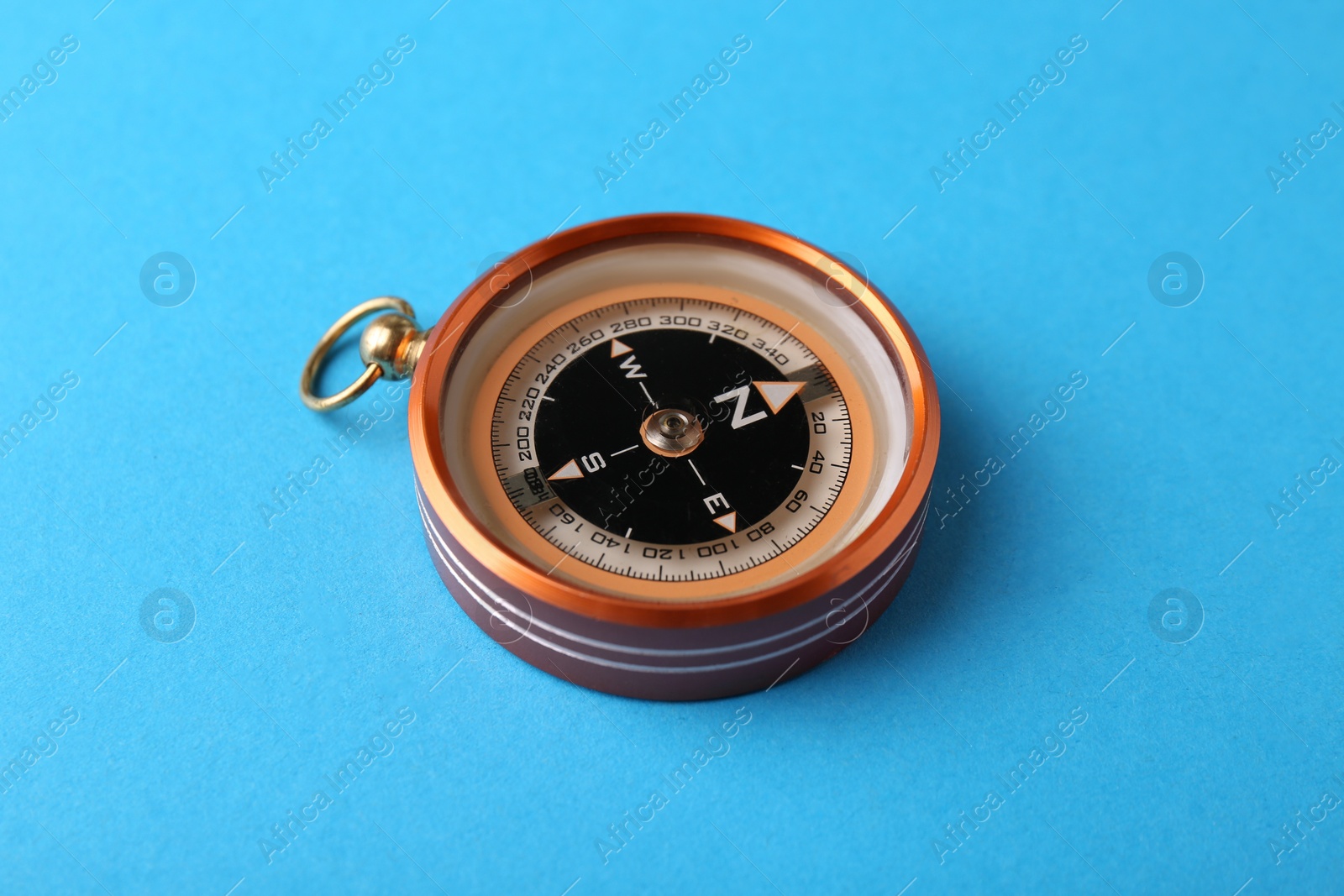 Photo of One compass on light blue background. Tourist equipment