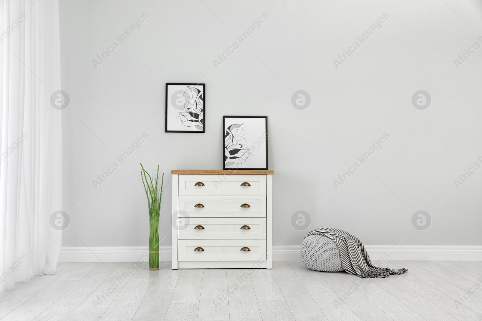 Photo of Stylish room interior with chest of drawers and space for design on light wall