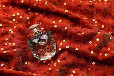 Photo of Luxury perfume in bottle on red fabric with sequins, top view