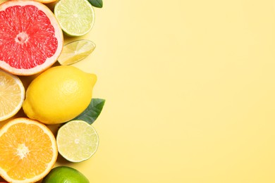 Photo of Different cut and whole citrus fruits on yellow table, flat lay. Space for text