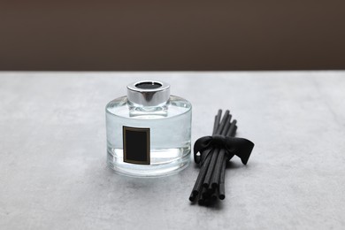 Photo of Reed sticks near glass bottle with aromatic liquid on gray marble table