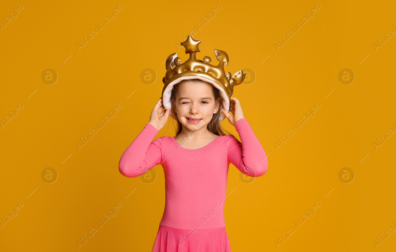 Photo of Cute girl in inflatable crown on yellow background. Little princess