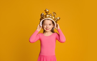 Photo of Cute girl in inflatable crown on yellow background. Little princess