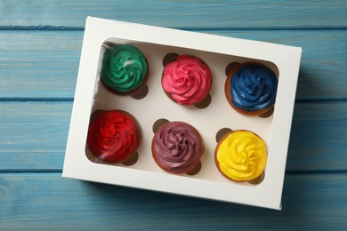 Box with different cupcakes on light blue wooden table, top view