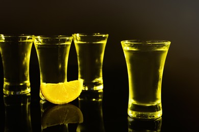 Shot glasses of vodka with lemon slice on dark background