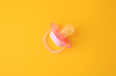 One new baby pacifier on orange background, top view