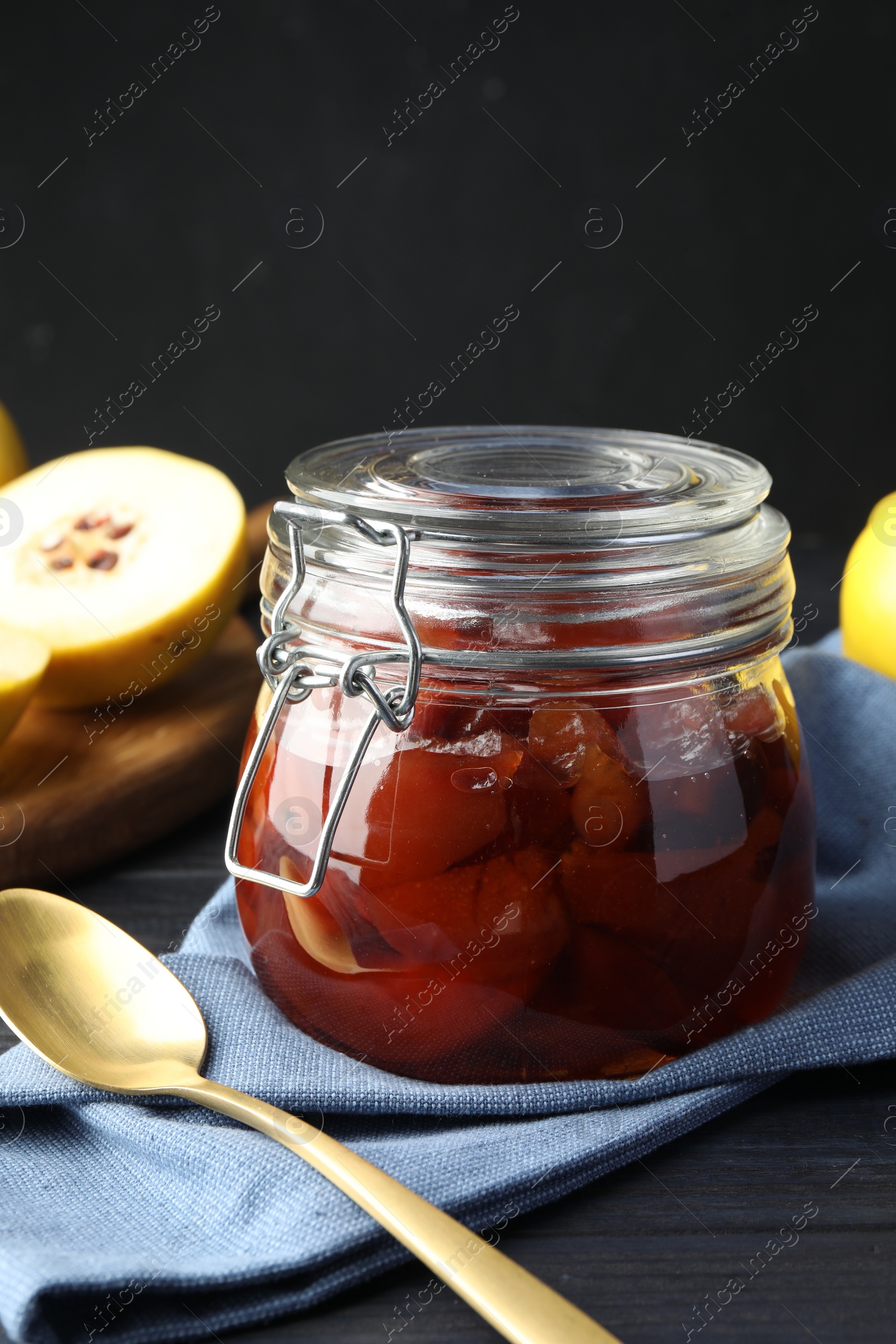 Photo of Quince jam in glass jar, spoon and fresh raw fruits on grey table, closeup