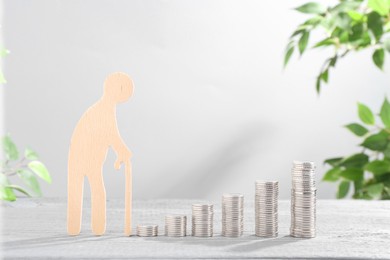 Photo of Pension savings. Figure of senior man and stacked coins on grey wooden table