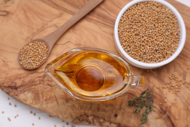 Photo of Jug of natural oil and mustard seeds on wooden table, flat lay